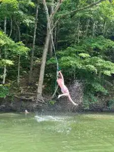 boy swinging off a rope swing over the lake