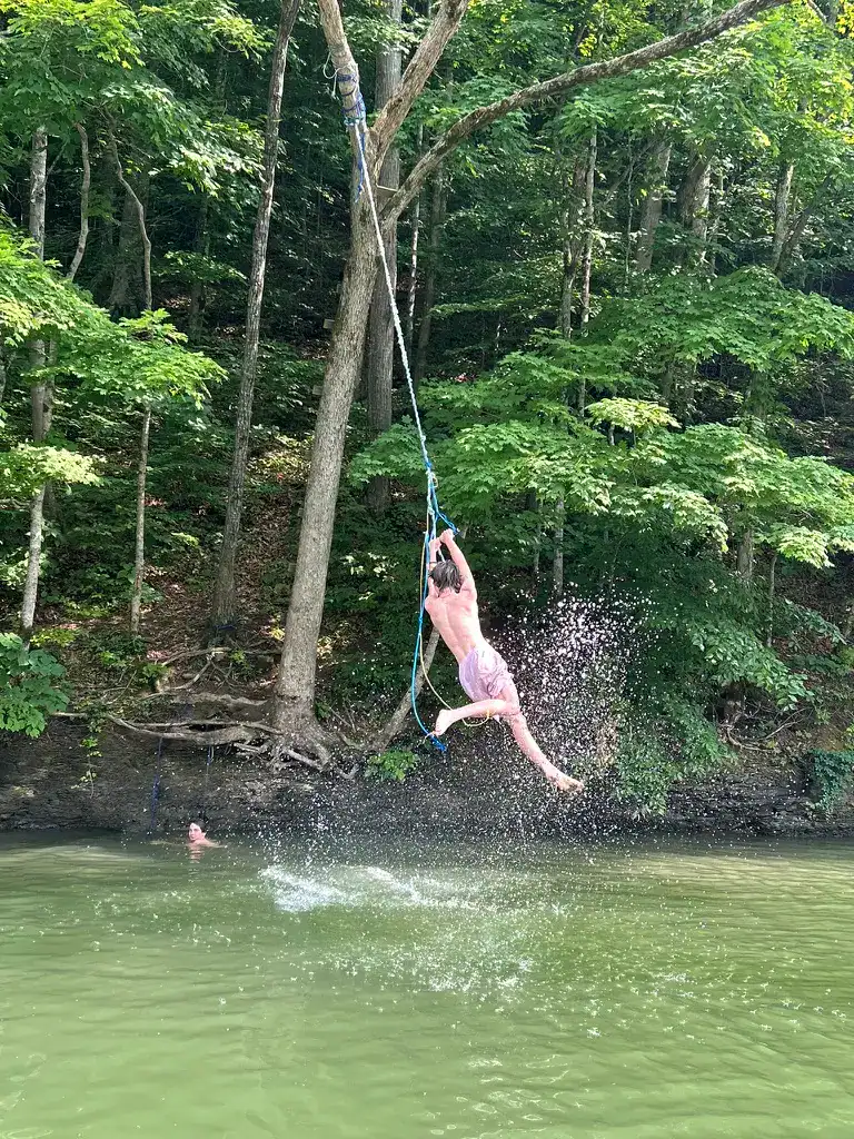 boy swinging off a rope swing over the lake