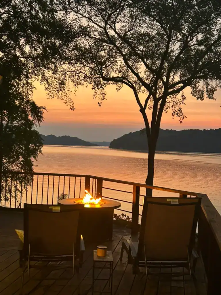 Sunset over the lake with lounge chairs silhouetted on a porch in front of a gas fireplace.