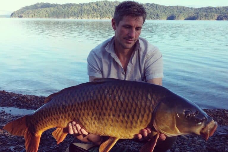 Man holding large carp fish on the shoreline of the lake
