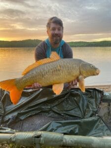 Man holding colorful mirror carp with the sunset and lake in the background