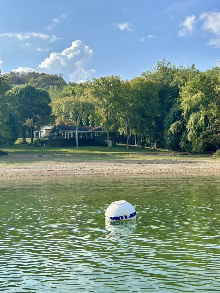 white buoy bobbing in still water in front of a lake house.