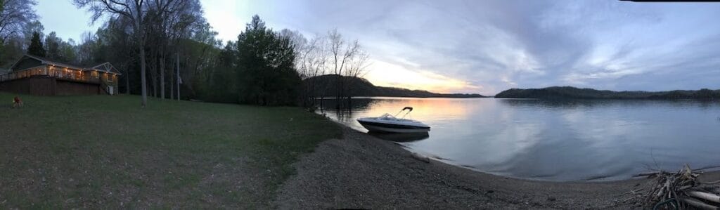 Sunset view of lake with boat at shore and illuminated lake house