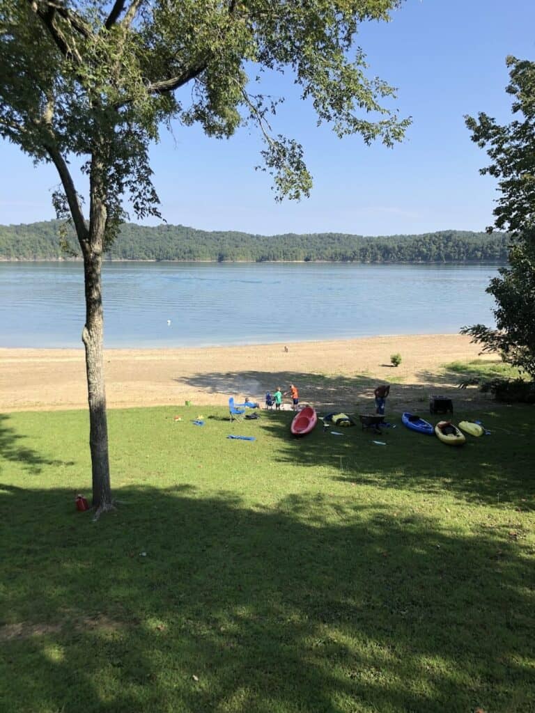 grassy yard with floats and toys on beach in front of lake.