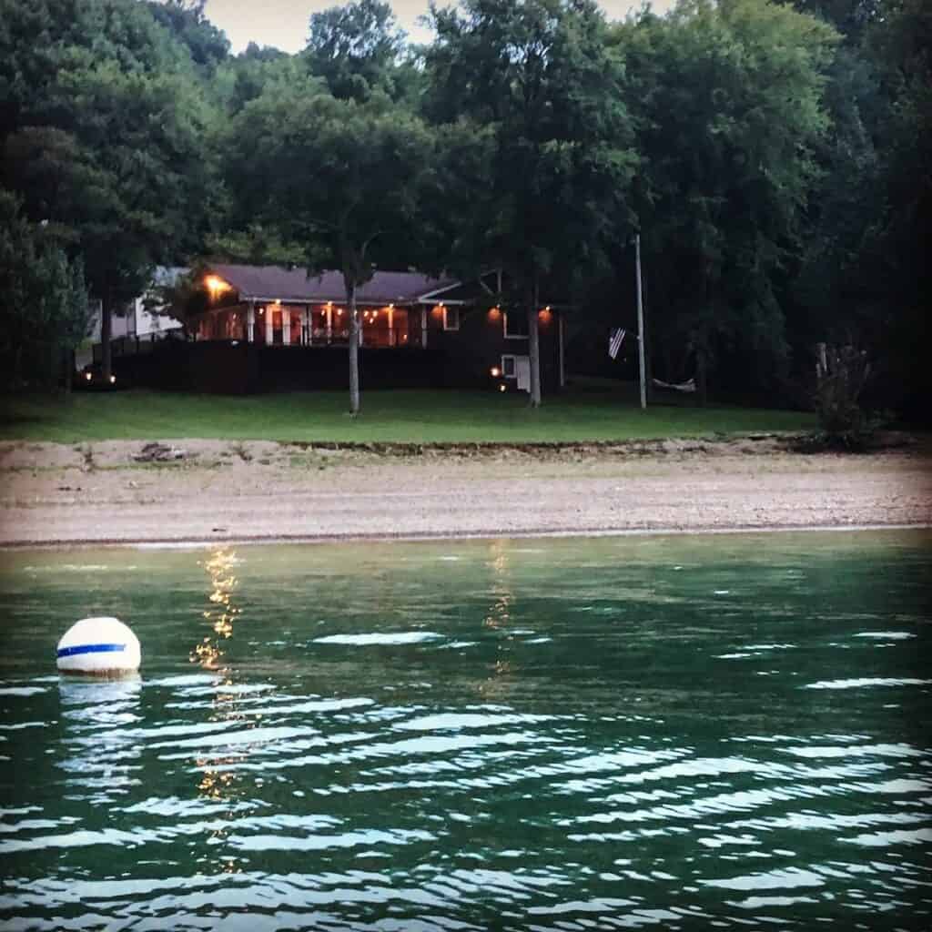 white buoy in water in front of illumintated lake house in evening.