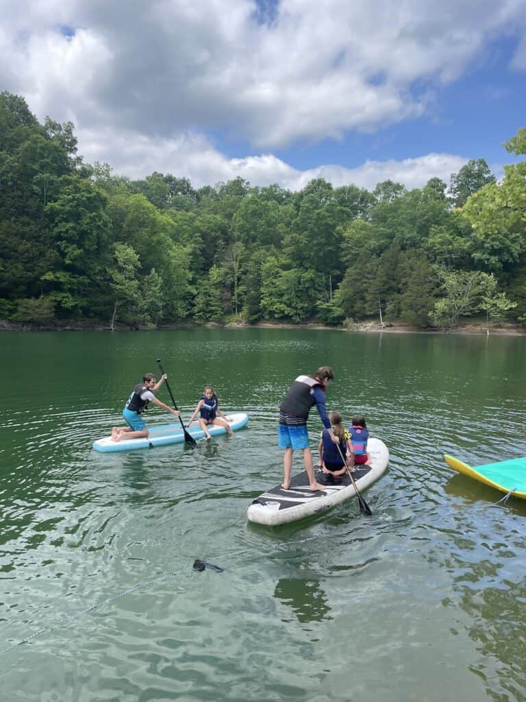 Many kids on 2 paddleboards playing on the water.