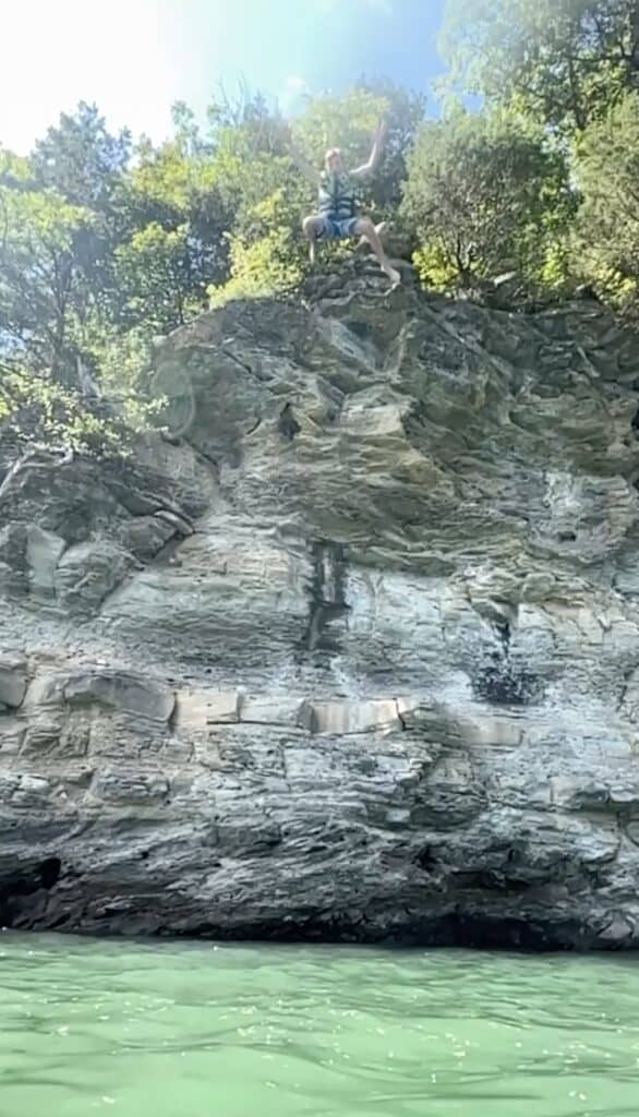 A boy jumping off a tall cliff into the water.