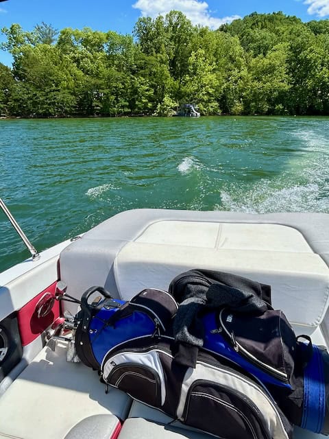 Back of a boat in the water with golf clubs sitting on the seat.