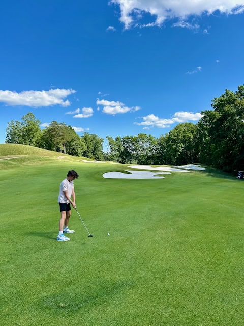 Boy putting with sand traps in the backgound.